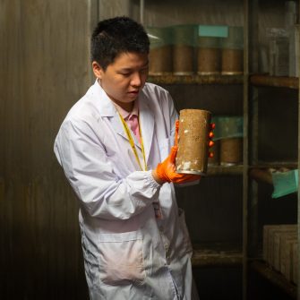 Student in lab coat holds cement cylinder in cool room.